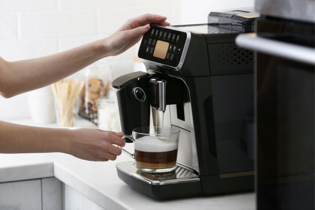 Pessoa com mão em máquina de café e segurando uma caneca com café