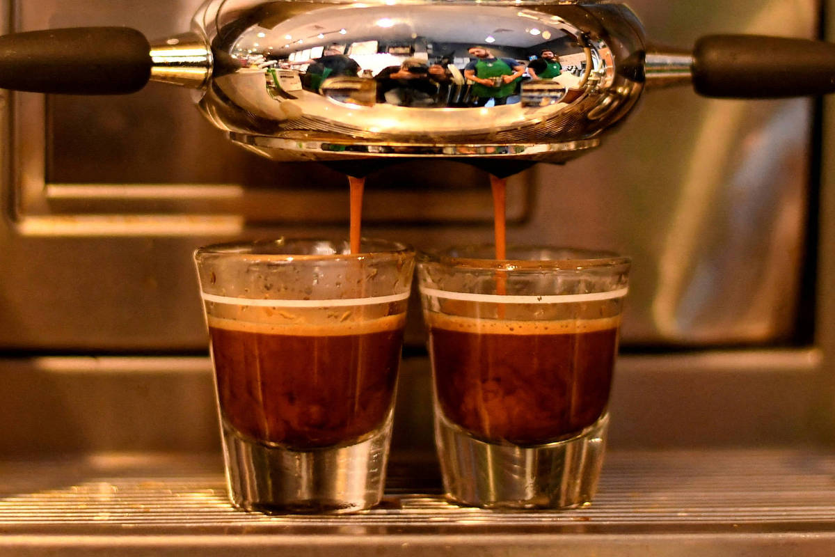 A imagem mostra uma máquina de café espresso em funcionamento, com dois copos pequenos de café sendo preenchidos.