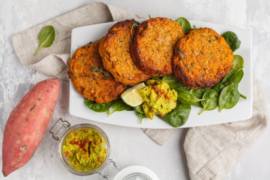Hambúrgueres de batata-doce e quinoa em cima de uma travessa branca  acompanhado com folhas de espinafre