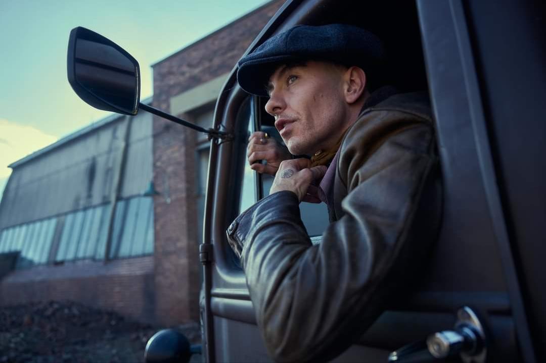 personagem-de-peaky-blinders-em-caminhao-antigo-usando-boina-e-casaco-de-couro-em-cenario-industrial