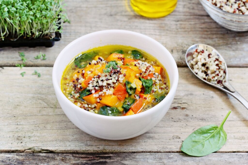 Bowl com sopa de abóbora, espinafre e legumes, coberta com quinoa tricolor cozida