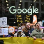 Grupo de manifestantes segura cartazes e faixa amarela em frente à fachada com logo do Google. Placas exibem mensagens como