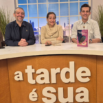 Sonia Abrão em estúdio de TV ao lado de dois apresentadores, durante entrevista sobre sua carreira e o lançamento de livro, participação que antecede sua presença confirmada na Expo Empreendedor 2026.