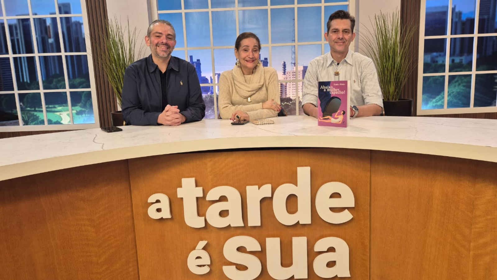 Sonia Abrão em estúdio de TV ao lado de dois apresentadores, durante entrevista sobre sua carreira e o lançamento de livro, participação que antecede sua presença confirmada na Expo Empreendedor 2026.
