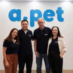 Equipe da APet reunida na sede da empresa, diante da identidade visual da marca.